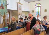 Children doing Stations of the Cross with Fr. Emil and catechism teacher Pat Gawaziuk. In the background are imitation "stained glass" crosses, which the children made to decorate church windows.